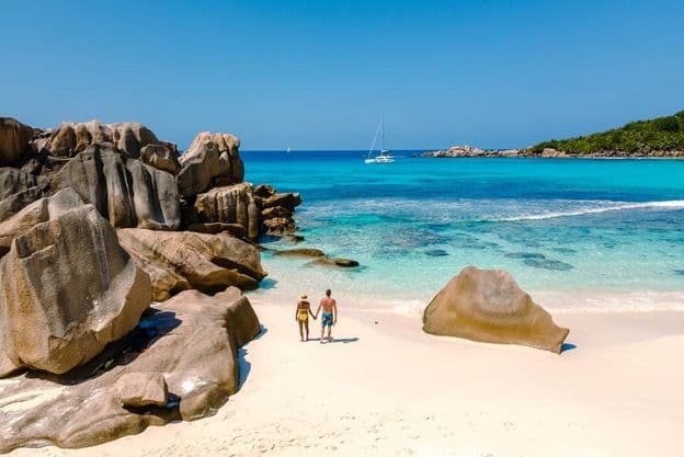 Zwei Reisende gehen am weichen weißen Sandstrand von Anse Cocos Beach auf den Seychellen spazieren.