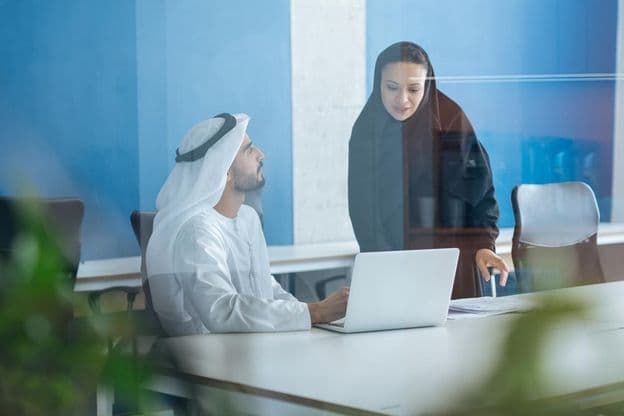 Ein Mann und eine Frau in traditioneller Kleidung arbeiten in einem Geschäftsbüro in Dubai.