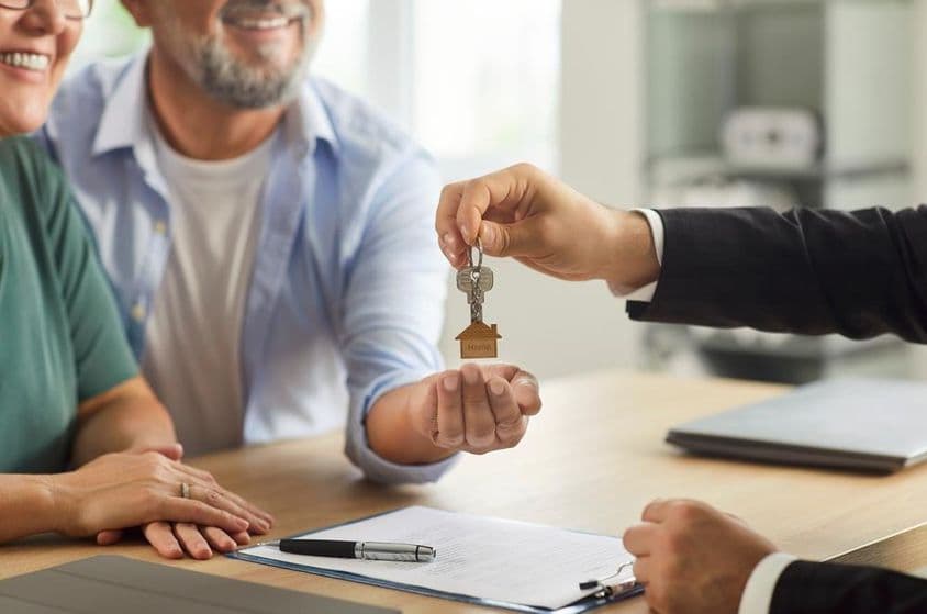 Ein Immobilienmakler übergibt einem lächelnden älteren Paar die Schlüssel.