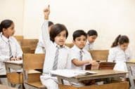 Glückliches indisches Schulkind hebt die Hand