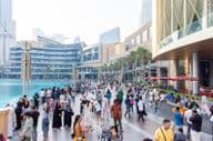Eine vielfältige Menschenmenge aus Touristen und Einheimischen geht entlang der belebten Uferpromenade vor der Dubai Mall.