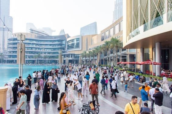 Eine vielfältige Menschenmenge aus Touristen und Einheimischen geht entlang der belebten Uferpromenade vor der Dubai Mall.
